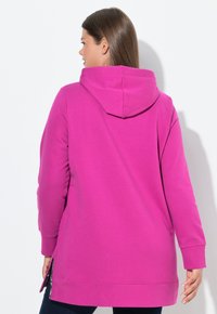Felpa cappuccio fucsia con maniche lunghe, fessure laterali e tessuto morbido. Ha un aspetto rilassato e lunghezza fino ai fianchi.