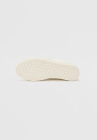 Semelle de sneaker blanche avec un motif texturé en formes de diamant. Matériau en caoutchouc lisse, bords légèrement arrondis et profil plat.
