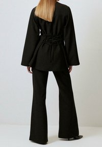 Sort belted top med flagrende ærmer og indsnævret talje, parret med matchende flagrende bukser. Materialet ser glat ud med en struktureret design.