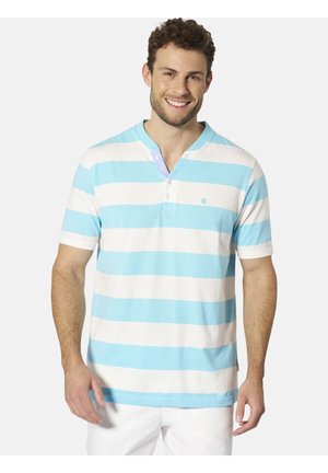 Mann lächelnd, trägt ein kurzärmeliges Poloshirt mit breiten horizontalen hellblauen und weißen Streifen sowie weiße Hosen.