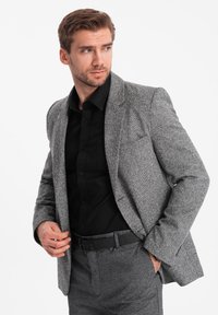 Grå herringbone-blazer med en slät textur, enfickad, skräddarsydd passform, kombinerad med en svart skjorta och matchande byxor.