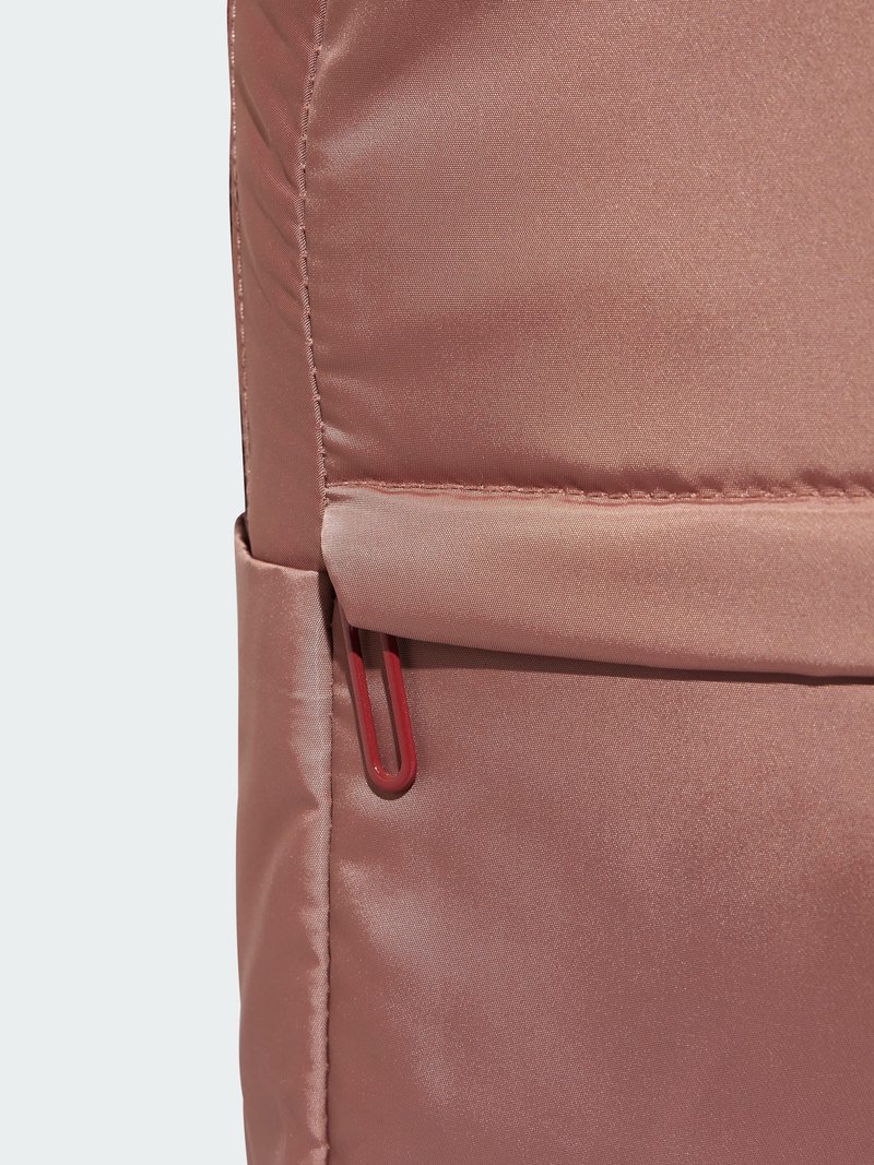 Dunkelrosa Stoff-Rucksack mit einer glatten Satin-Oberfläche, ausgestattet mit einem roten Reißverschlussanhänger und einer Vordertasche mit Klappenverschluss.