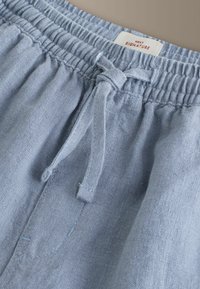 Pantalon en lin bleu clair avec taille élastique et lien noué, montrant la poche supérieure et la texture du tissu.
