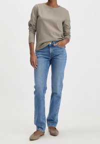 Beige långärmad topp med rund halsringning, kombinerad med ljusblå jeans med raka ben. Skorna är ljusbruna med en mjuk textur.