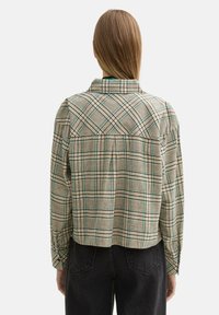 Camicia button-up tagliata in beige con motivo a scacchi verde e nero. Presenta un colletto a punta, maniche lunghe e un dettaglio a pieghe sul retro.