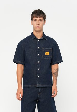 Short-sleeve denim shirt in dark blue; features button closure, chest pocket with orange label, and contrasting stitching details.