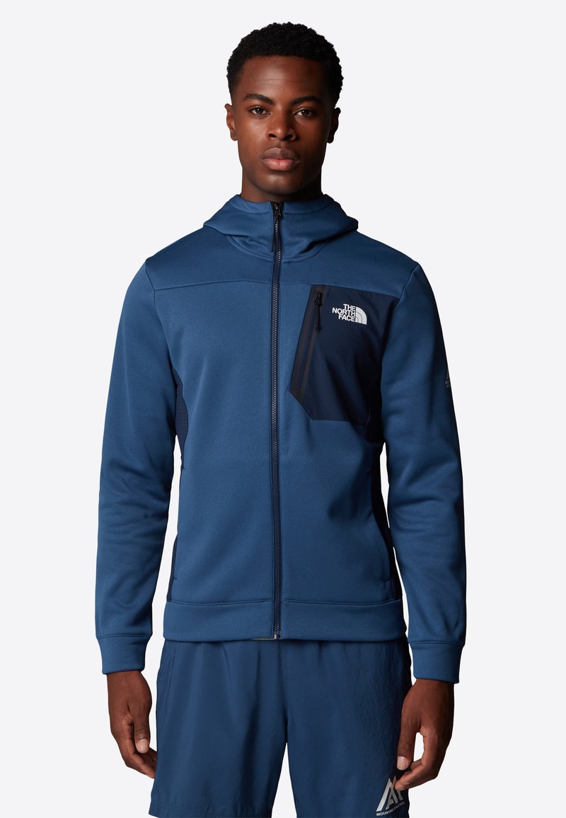 Navyblauwe rits hoodie van zacht materiaal met een voorzak met rits en contrasterende donkerblauwe accenten. Voorzien van een capuchon en geribde manchetten.