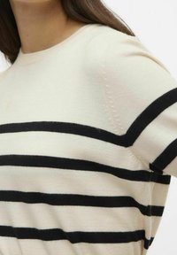 Slonovinový pletený svetr s horizontálními černými pruhy, kulatým výstřihem a krátkými rukávy. Hladká textura s jemnými detaily na rameni.