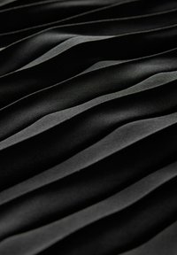 Czarna tkanina z teksturowanymi, falistymi fałdami tworzącymi dynamiczny wzór. Materiał wydaje się miękki z gładką powierzchnią, podkreślającą grę cienia i światła.