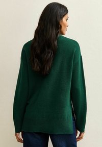 Zielony, oversize'owy sweter dzianinowy o teksturowanym wykończeniu, z obniżonymi ramionami i prostym dołem, noszony na ciemnej dżinsowej odzieży.