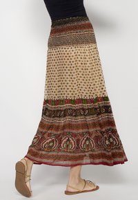 Maxi skirt featuring a smocked waistband, layered pastel fabric with intricate floral patterns and earthy tones of red, green, and beige.