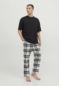 Juoda trumpomis rankovėmis marškinėliai derinami su baltomis ir juodomis languotomis pižamos kelnėmis, pasižyminčiomis tiesiu kirpimu ir minkštu audinio paviršiumi.