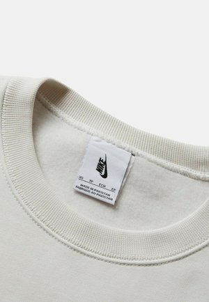 Lichtbeige sweatshirt kraag met geribbelde textuur. Inclusief een Nike logo label, waarop maat en herkomstland staan. Zacht stof zichtbaar.