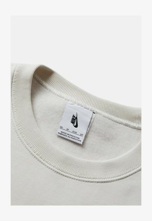 Lichtbeige sweatshirt kraag met geribbelde textuur. Inclusief een Nike logo label, waarop maat en herkomstland staan. Zacht stof zichtbaar.