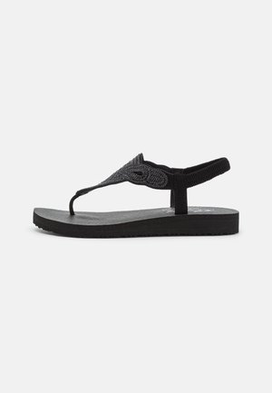 Sort flad sandal med perlebesat thongsrem og elastisk bagrem på tekstureret sål, vist i sideprofil på hvid baggrund.