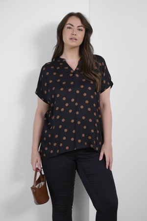 Haut noir avec des pois marron, manches courtes et décolleté en V. Associé à un pantalon noir et un petit sac à main marron.