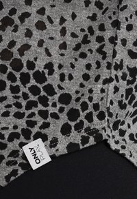 Šedá látka s černým vzorem leoparda, obsahující viditelnou štítek. Okraje mají úhledné švy a příjemný, texturovaný povrch.
