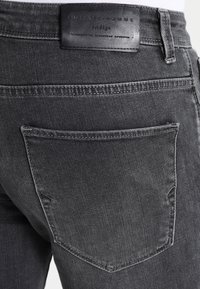 Grå denimjeans med en klassisk passform, med en läderlapp på midjebandet och en enda bakficka med synliga sömdetaljer.