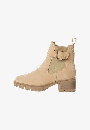 Suède enkellaars in lichtbeige met elastische zijkanten, een gouden gespaccent, en een gestructureerde blokhak. Gecontourde, duurzame rubbersolo.