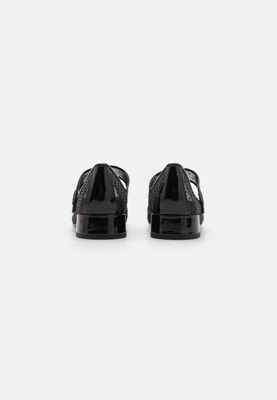 Schwarze Lacklederschuhe mit ausgeschnittenem Design, ausgestattet mit einem niedrigen Blockabsatz und einer glatten, glänzenden Oberfläche. Die Rückansicht zeigt perforierte Details.