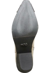 Beige högklackad skosula med en texturerad svart gummiyta, med rund tå och ett extra mönster för grepp.