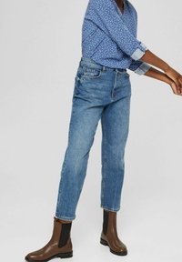 Jeans di denim azzurro con una vestibilità comoda, abbinati a una camicia blu con pois e stivali alla caviglia marroni con pannelli laterali in elastico neri.