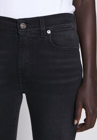 Jeans neri con vestibilità slim, realizzati in denim. Presentano una chiusura con bottone, tasche frontali e dettagli di cucitura lungo le cuciture.