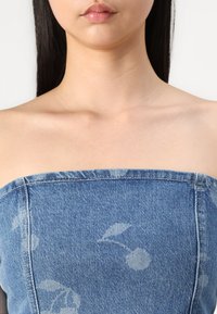 Blå denim strapless topp med et svakt blomstermønster, som viser en strukturert passform med sømdetaljer langs kantene.