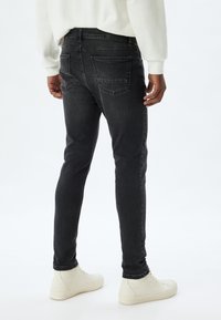 Jeans de mezclilla gris con un corte slim, con bolsillos traseros y detalles de costura sutiles. Llevados con zapatillas blancas, sobre un fondo neutro.