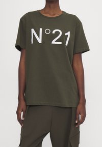 Camiseta de algodón verde oliva con mangas cortas y cuello redondo, con un gran texto estampado en blanco "N°21" en el frente. Diseño de corte recto.