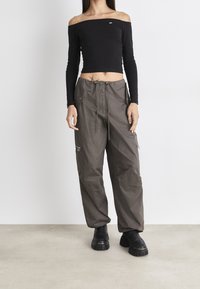 Schwarzes Off-Shoulder Langarm-Oberteil kombiniert mit lässigen, olivgrünen Cargo-Hosen mit Taschen und Kordelzugbund, getragen mit schwarzen Plateau-Stiefeln.