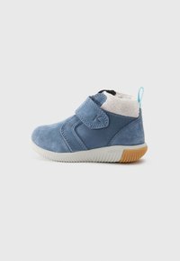 Blaue Wildleder-Stiefelette mit einem flauschigen Innenfutter, verstellbarem Riemen und cremefarbener Sohle mit strukturiertem Griffigkeitsmuster. Der Rücken hat einen Schlaufenakzent.