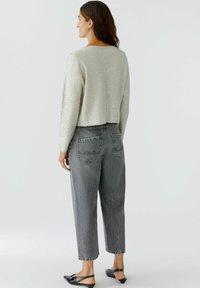 Pull en argent texturé avec des manches longues, associé à un jean en denim gris taille haute avec des poches arrière et une coupe décontractée.
