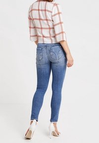 Modré skinny džíny s vybledlým vzhledem, jemným žebrováním, dvěma zadními kapsami, v kombinaci s bílou kostkovanou blůzou s oranžovými pruhy.