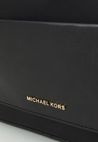 Černá kabelka s texturovaným koženým designem, se zlatým logem "MICHAEL KORS" a čistými detaily šití.