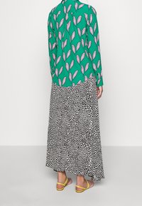 Blusa verde a stampa floreale con maniche lunghe, abbinata a una gonna maxi a fantasia bianca e nera. Indossata con sandali gialli.