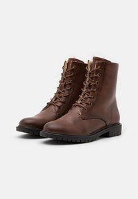Botas de tornozelo em pele castanha com bico arredondado, atacador frontal e ilhós de metal. Sola de borracha texturada para maior aderência.