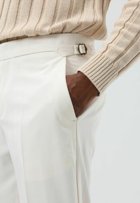 Crèmekleurige broek met een strak ontwerp, voorzien van een zijzak en een decoratieve gesp in de taille. De textuur is glad en op maat gemaakt.