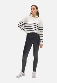 Suéter blanco con rayas marinas y cuello con cremallera, combinado con leggings negros y zapatillas blancas. Texturas suaves y formas ajustadas.