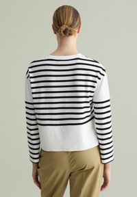 Gestreiftes Langarmshirt in Weiß und Schwarz, mit horizontalen Streifen, Rundhalsausschnitt, kontrastierendem unteren Bereich und lockerer Passform.