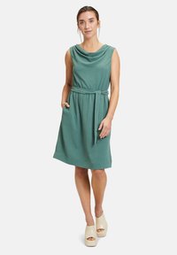 Ärmelloses grünes Kleid mit einem Cowl-Ausschnitt, Taillengürtel und Taschen. Aus strukturiertem Stoff gefertigt, mit einer lockeren Passform.