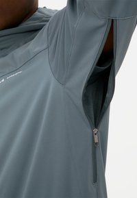T-shirt de sport gris avec une poche latérale zippée, fabriqué en tissu lisse et léger. Doté de détails de couture subtils et d'une coupe décontractée.