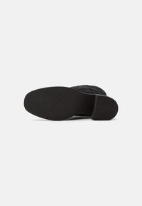 Botín negro de ante con suela de goma texturizada. Presenta una punta redondeada y un diseño minimalista para un estilo versátil.