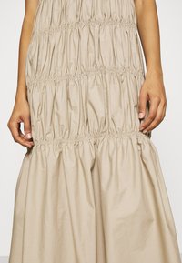 Robe en coton beige avec un design smocké et des fronces horizontales, créant une apparence texturée. L'ourlet est plein et fluide.