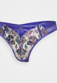 Lingerie violet avec broderies florales en bleu, vert et violet ; présente un tissu transparent, des éléments décoratifs et des bretelles contrastantes.