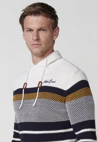 Suéter a rayas en blanco, azul marino y mostaza con capucha. Textura de punto, presenta un cordón y un logo en el pecho. Estilo casual.