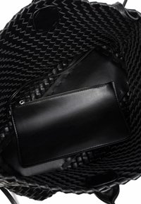 Czarna pleciona torba typu tote o błyszczącym wykończeniu. Wnętrze wyposażone w gładką skórzaną kieszeń na zamek dla lepszej organizacji.