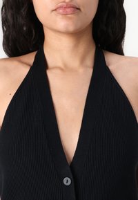 Zwarte geribbelde halterneck top met een diepe V-halslijn, voorzien van een enkele knoopsluiting en textuurstof.