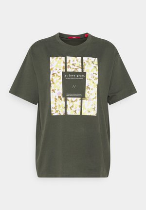 Olivgrünes Baumwoll-T-Shirt mit kastiger Form. Verfügt über ein florales Grafikdesign in Gelb und Weiß, begleitet von einem bedruckten schwarzen Etikett.