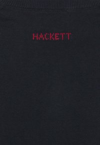 Černá pletená tkanina s červeným vyšívaným textem velkými písmeny "HACKETT" blízko horního středu.